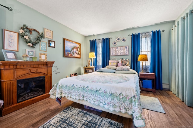 61 Harrington St, Meriden, CT 06451 - bedroom featuring a glass covered fireplace, a baseboard radiator, a textured ceiling, and wood finished floors