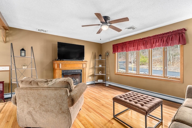living room with a textured ceiling, a baseboard heating unit, a fireplace, and a ceiling fan