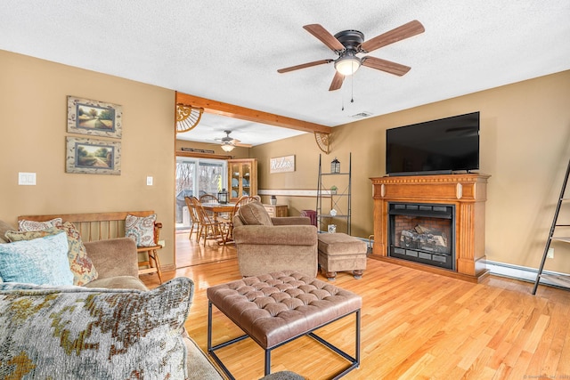living room with ceiling fan, a textured ceiling, wood finished floors, and a fireplace