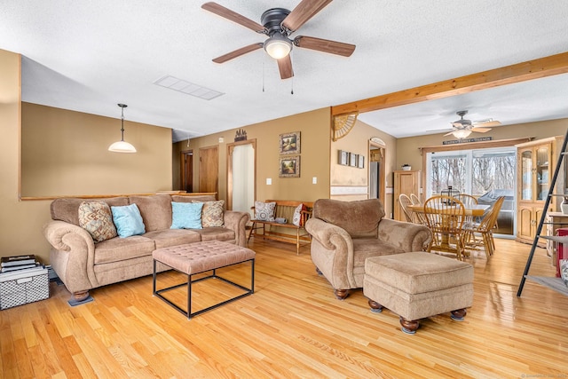 living room featuring light wood-type flooring, ceiling fan, visible vents, and a textured ceiling