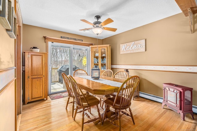 dining area with a wood stove, ceiling fan, a textured ceiling, light wood-type flooring, and a baseboard radiator