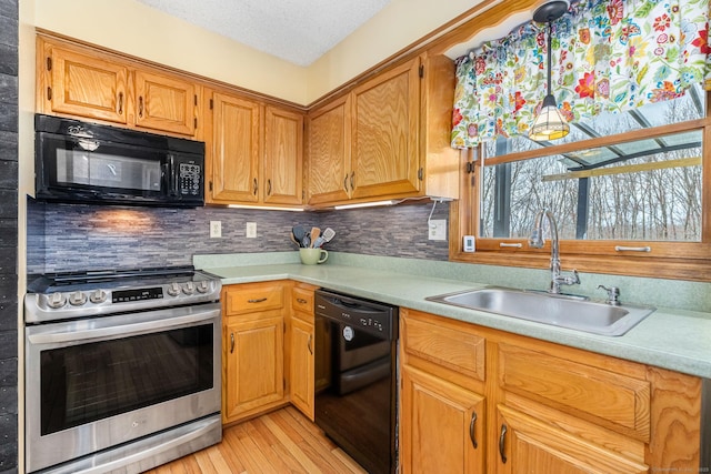 kitchen with light wood-type flooring, light countertops, black appliances, decorative backsplash, and a sink