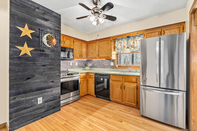 kitchen with brown cabinetry, tasteful backsplash, black appliances, light countertops, and a sink