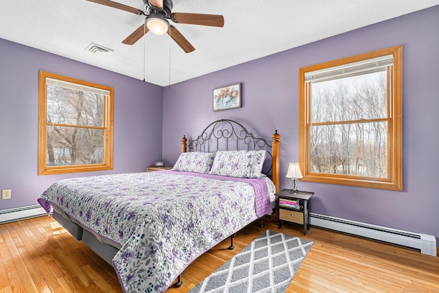 bedroom featuring a baseboard radiator, ceiling fan, wood-type flooring, and visible vents