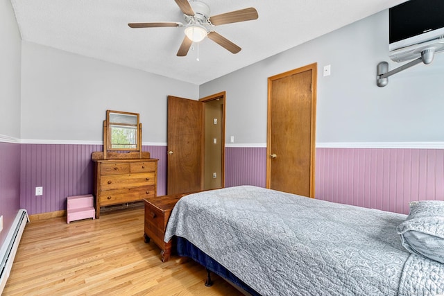 bedroom featuring baseboards, a ceiling fan, wainscoting, a baseboard radiator, and wood finished floors