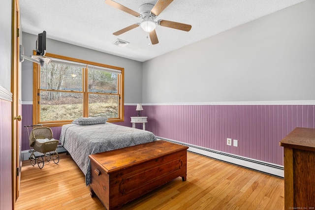 bedroom with visible vents, a wainscoted wall, wood-type flooring, and a baseboard radiator
