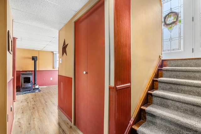 stairs with a wood stove, a drop ceiling, a wainscoted wall, wood finished floors, and wood walls