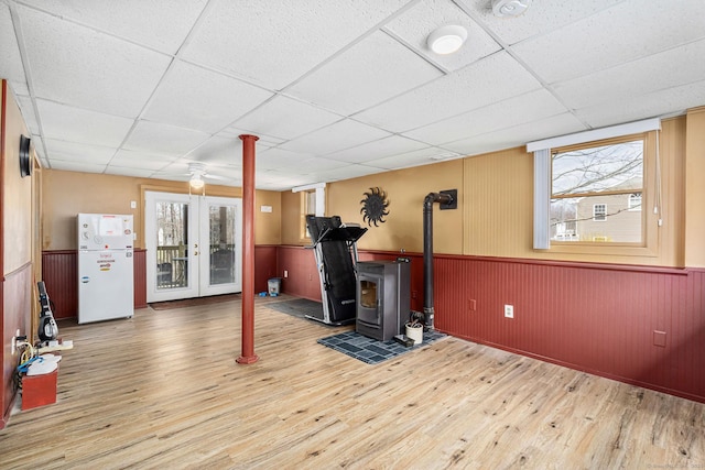 basement with a wood stove, a paneled ceiling, freestanding refrigerator, and wood finished floors