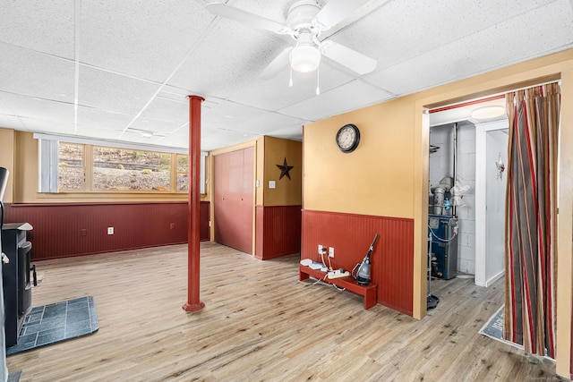 basement with a wainscoted wall, ceiling fan, a paneled ceiling, and wood finished floors