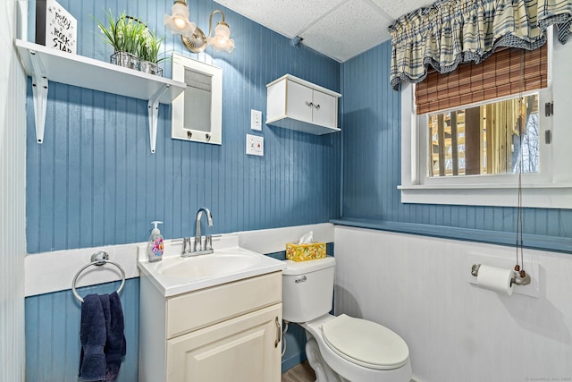 half bath with vanity, a drop ceiling, and toilet