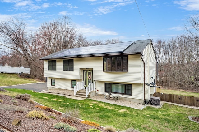 split foyer home featuring a front yard, fence, and solar panels
