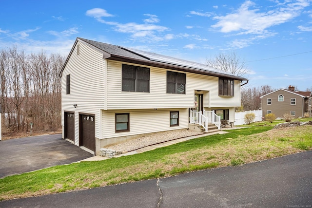bi-level home with driveway, a front lawn, a garage, fence, and roof mounted solar panels