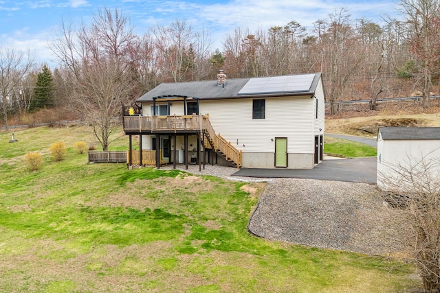 back of house featuring roof mounted solar panels, a wooden deck, a yard, stairway, and a chimney