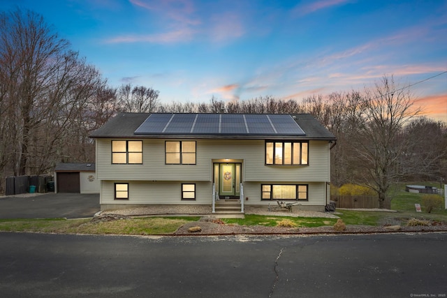 bi-level home with an outbuilding, a garage, roof mounted solar panels, and fence