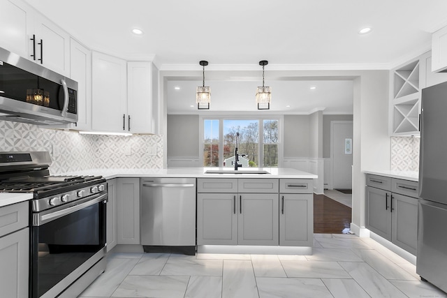 kitchen featuring appliances with stainless steel finishes, a sink, a peninsula, gray cabinetry, and ornamental molding