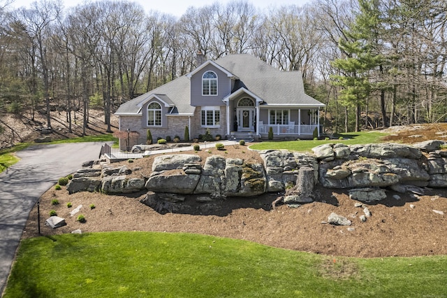 view of front facade with a porch, a chimney, stone siding, and a front lawn