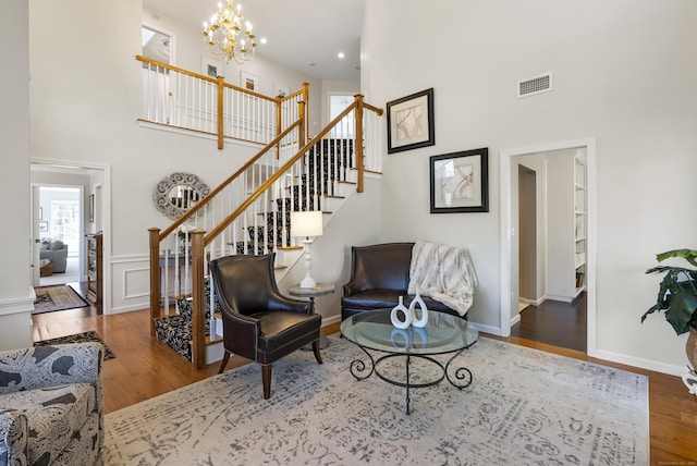 living area with a notable chandelier, visible vents, wood finished floors, and a towering ceiling