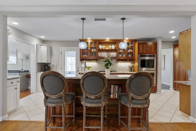 kitchen featuring backsplash, light tile patterned floors, visible vents, and glass insert cabinets