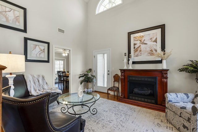 living room with a ceiling fan, visible vents, a fireplace, wood finished floors, and a high ceiling