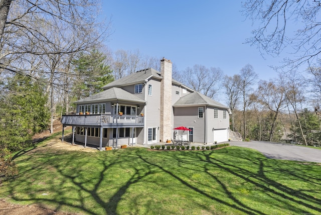 back of property featuring a garage, a wooden deck, roof with shingles, a chimney, and driveway