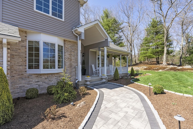doorway to property featuring brick siding, a yard, and covered porch