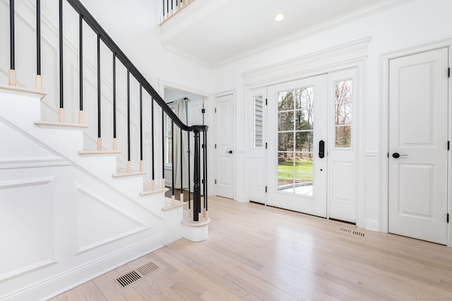 foyer with wood finished floors, ornamental molding, visible vents, and stairway