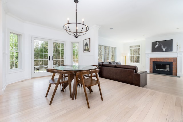 dining area with an inviting chandelier, light wood-type flooring, a brick fireplace, french doors, and plenty of natural light