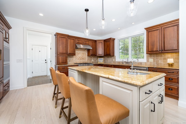 kitchen with light stone counters, a center island, under cabinet range hood, decorative backsplash, and a sink