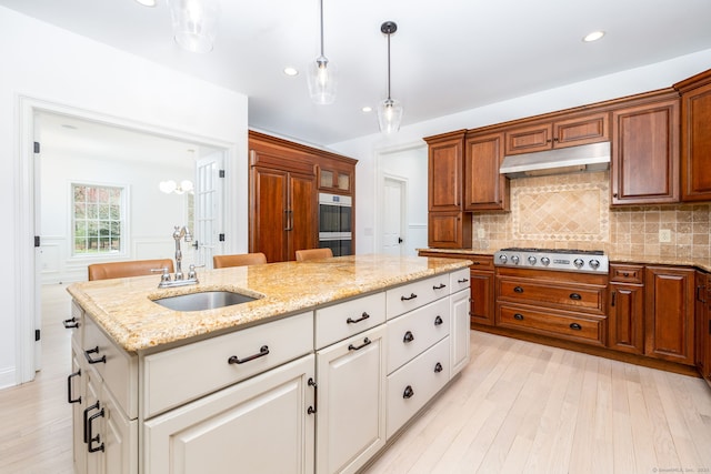 kitchen with tasteful backsplash, a sink, light wood-type flooring, under cabinet range hood, and stainless steel gas stovetop