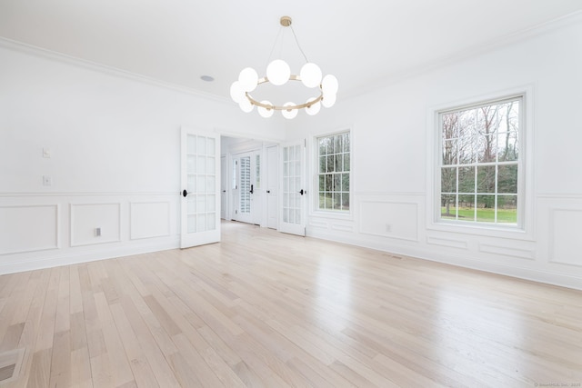 unfurnished dining area with a decorative wall, ornamental molding, light wood-type flooring, and a chandelier