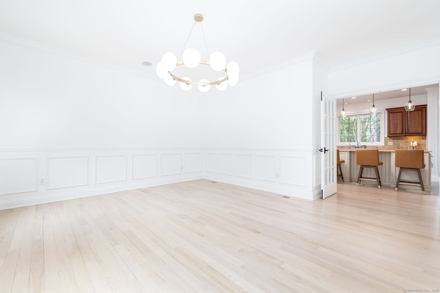 unfurnished dining area with a notable chandelier, a decorative wall, ornamental molding, light wood-style floors, and a wainscoted wall