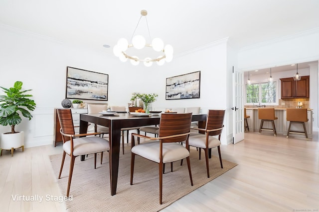 dining space featuring ornamental molding, light wood-style flooring, and an inviting chandelier