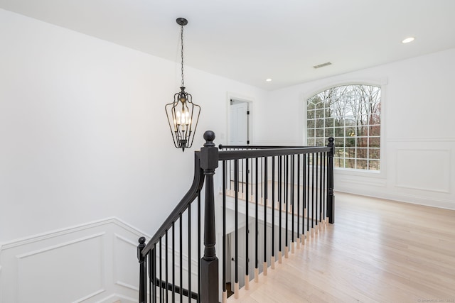 stairs with a chandelier, wainscoting, visible vents, a decorative wall, and wood finished floors