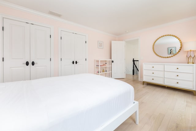 bedroom with baseboards, ornamental molding, light wood-style floors, visible vents, and multiple closets