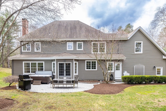 rear view of house with a hot tub, a yard, a chimney, a patio, and french doors
