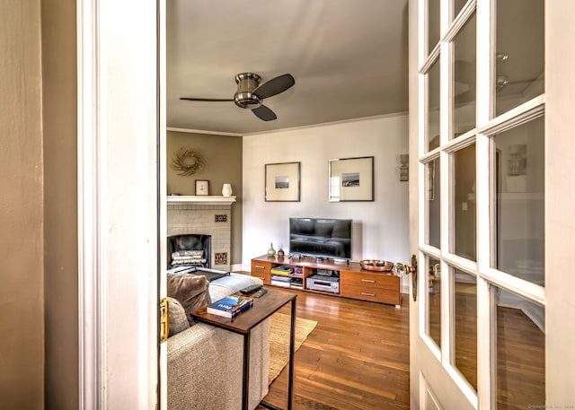 living area with ceiling fan, wood finished floors, a fireplace, and crown molding