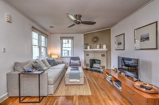 living area featuring a ceiling fan, ornamental molding, wood-type flooring, a fireplace, and baseboards