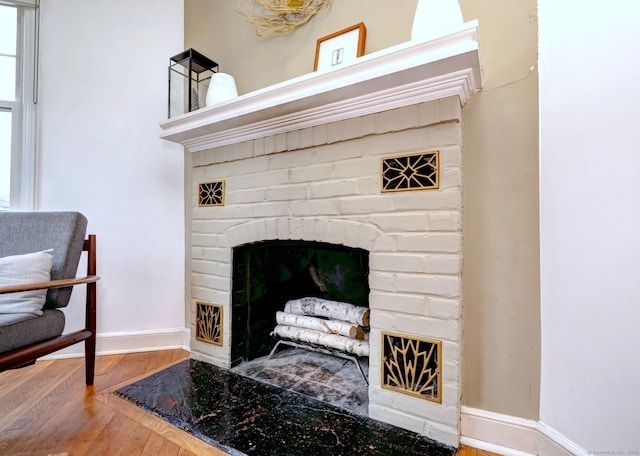 detailed view of a fireplace, wood finished floors, and baseboards