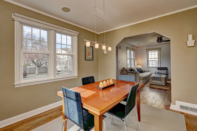 dining area with hardwood / wood-style flooring, baseboards, arched walkways, a ceiling fan, and crown molding