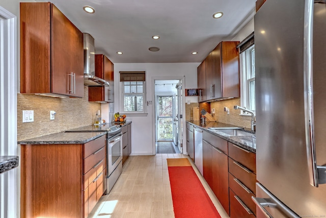 kitchen with stainless steel appliances, wall chimney range hood, a sink, healthy amount of natural light, and recessed lighting