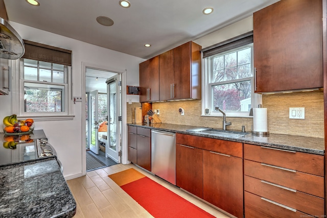 kitchen with a sink, stainless steel dishwasher, healthy amount of natural light, dark stone countertops, and recessed lighting