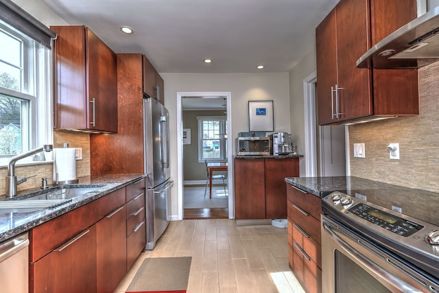 kitchen with wall chimney exhaust hood, appliances with stainless steel finishes, a sink, decorative backsplash, and recessed lighting