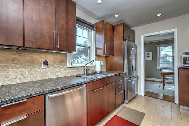 kitchen featuring stainless steel appliances, a sink, decorative backsplash, recessed lighting, and dark stone countertops
