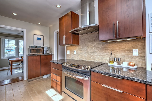 kitchen with wall chimney exhaust hood, stainless steel electric stove, dark stone counters, tasteful backsplash, and recessed lighting