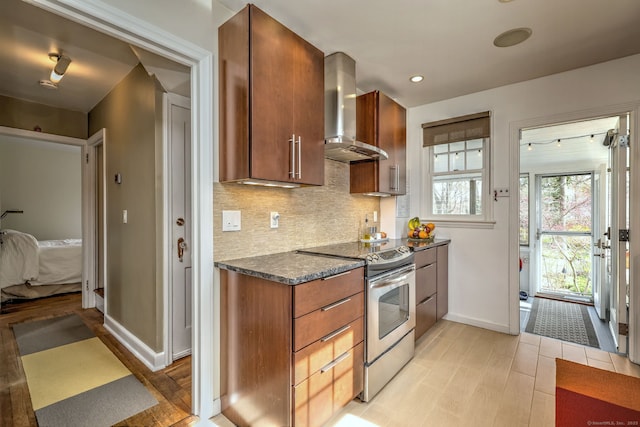 kitchen with stainless steel range with electric stovetop, wall chimney exhaust hood, baseboards, decorative backsplash, and light wood-style floors