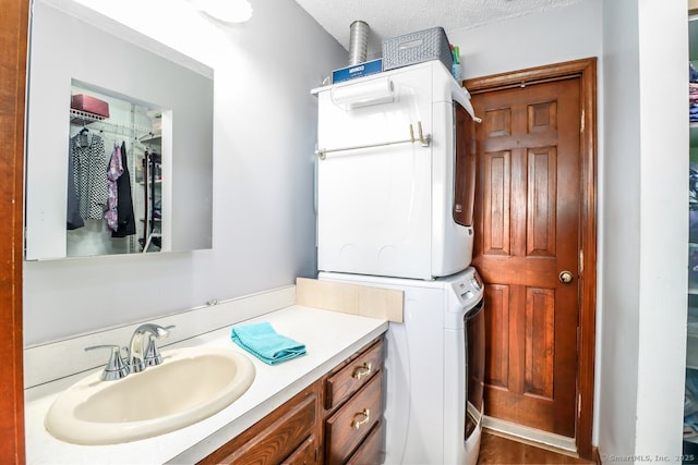 bathroom with a textured ceiling, stacked washer / drying machine, and vanity