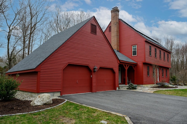 view of front of house with a chimney, driveway, an attached garage, and roof with shingles