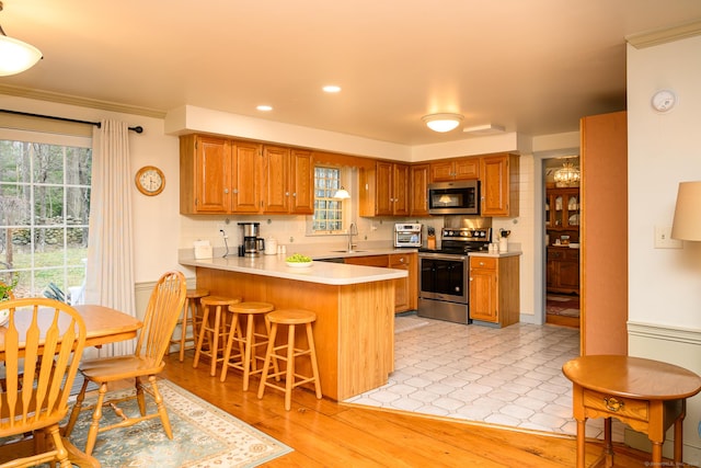 kitchen with brown cabinets, appliances with stainless steel finishes, a breakfast bar, light countertops, and a peninsula