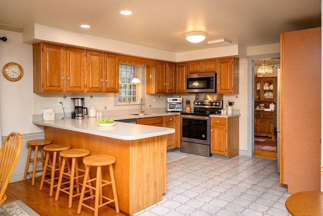 kitchen with a kitchen breakfast bar, a sink, stainless steel appliances, light countertops, and a peninsula