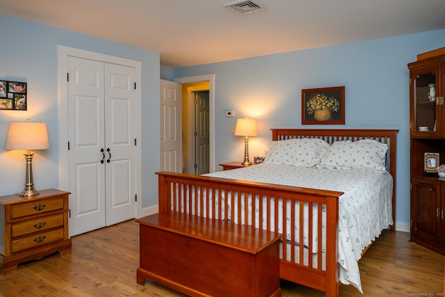bedroom with wood finished floors, visible vents, and a closet